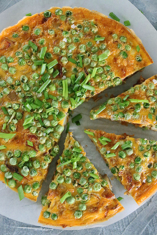 这是一幅西班牙玉米饼/肉馅煎蛋饼的图片，上面涂着绿色的豌豆和葱，三角形的自制西班牙早餐煎蛋卷